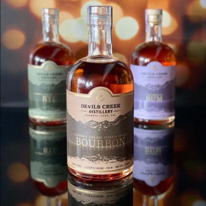 Devils Creek bourbon, rye, and rum — cream labels, mountain silhouette, gold flame